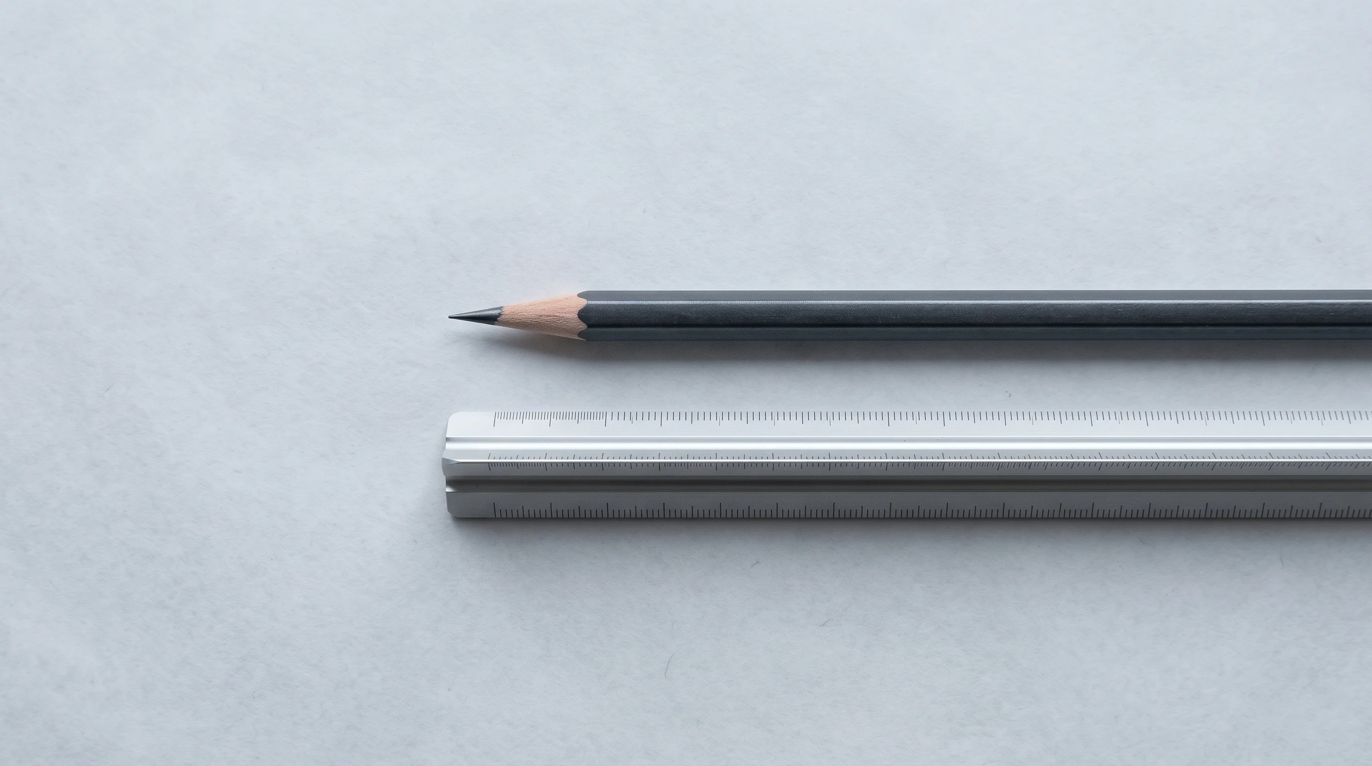 A freshly sharpened graphite pencil lying on blank trace paper beside a steel scale rule