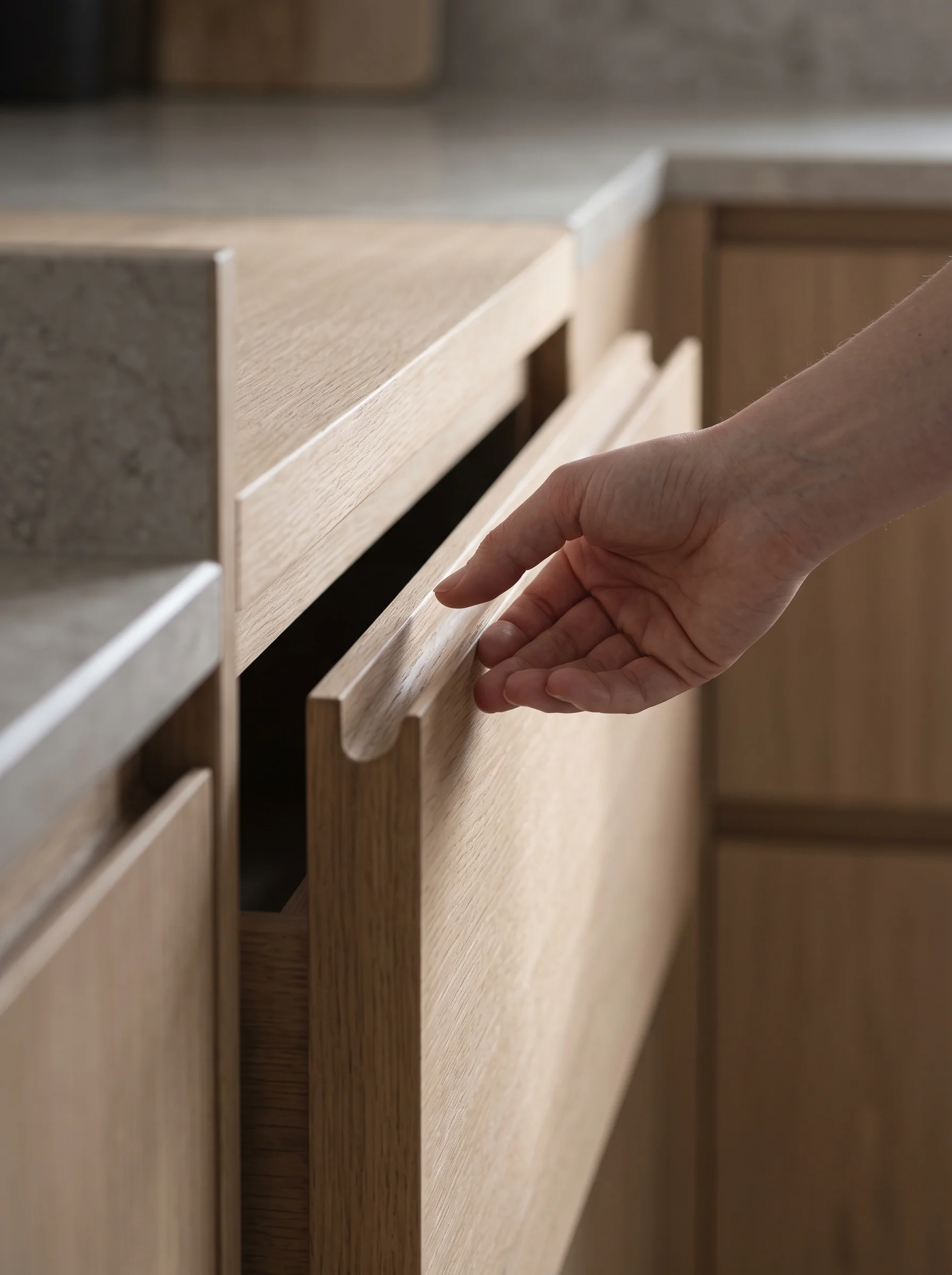A hand resting on the routed edge of a handleless drawer front, the shadow gap running true across matt cabinetry